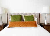 Thumbnail 3 of 34 - A bed with a white sheet and three pillows, two green and one orange.
