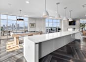 Thumbnail 29 of 60 - A modern kitchen with a long white island and a view of the city.