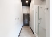 Thumbnail 14 of 24 - a hallway with white walls and a white tile floor with a glass shower door