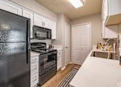 Thumbnail 7 of 31 - Galley kitchen with white cabinets and black appliances at Highland Park Apartments, Fort Worth
