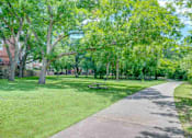 Thumbnail 3 of 25 - a sidewalk through a park with trees and a picnic table