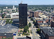 Thumbnail 1 of 107 - A tall building stands in the middle of a city intersection.