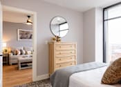 Thumbnail 90 of 106 - A bedroom with a bed, dresser, and a round mirror on the wall.