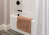 Thumbnail 29 of 38 - A white bathtub with a brown towel and a white shower curtain.