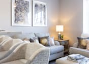 Thumbnail 20 of 38 - A living room with a grey sofa, a white armchair, a wooden coffee table, and two framed pictures on the wall.