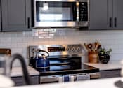 Thumbnail 11 of 84 - A modern kitchen with a black stove top and a black microwave above it.