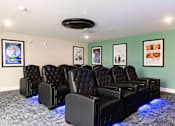 Thumbnail 28 of 50 - A row of black leather recliner chairs are lined up in a room with blue lights underneath them.