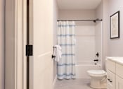 Thumbnail 16 of 50 - A white toilet sits in a bathroom next to a shower curtain.