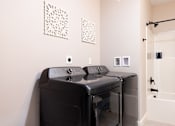 Thumbnail 15 of 50 - A black washing machine and dryer in a white laundry room.