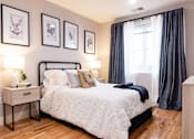Thumbnail 10 of 50 - A bedroom with a large bed, a nightstand with a plant, and framed pictures on the wall.