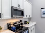 Thumbnail 105 of 106 - A modern kitchen with a black stove top and white cabinets.