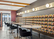 Thumbnail 28 of 99 - A restaurant with a long table and chairs with a wall of tiles behind it.