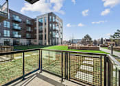 Thumbnail 60 of 99 - A balcony with a metal railing overlooks a grassy area and buildings.