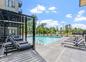 Thumbnail 91 of 103 - A pool area with sun loungers and a building in the background.