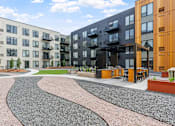 Thumbnail 86 of 103 - A modern apartment complex with a gravel courtyard in the foreground.