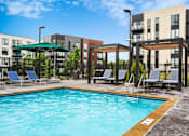 Thumbnail 3 of 55 - A swimming pool surrounded by chairs and a fence in front of apartment buildings.