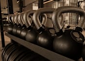 Thumbnail 64 of 85 - A rack of black kettlebells with 30 and 25 lb weights.