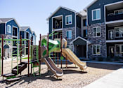 Thumbnail 21 of 34 - A playground with a green and tan slide in front of a building.
