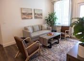 Thumbnail 6 of 34 - A living room with a grey couch, a brown chair, a coffee table, and two paintings on the wall.
