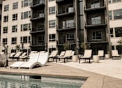 Thumbnail 70 of 85 - A pool area with sun loungers and apartment buildings in the background.