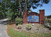 Thumbnail 1 of 10 - The entrance to The Cloisters with a blue sign on a brick wall. The Cloisters Apartments, 902 67th Avenue North, Myrtle Beach, SC