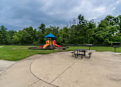Thumbnail 14 of 14 - A playground with a blue and yellow slide, picnic tables, and a concrete area.