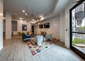 Thumbnail 10 of 30 - A community living room with two TVs, hanging lights, and seating near a door leading to an outdoor patio.