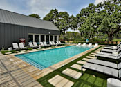 Thumbnail 3 of 30 - A refreshing swimming pool surrounded by green space with patios, lounge chairs, and large trees.