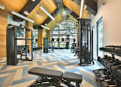 Thumbnail 6 of 30 - A modern gym with weights, cardio equipment, a TV, mirrors, a ceiling fan, an A-frame ceiling, and large windows with ample natural light.