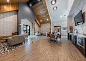 Thumbnail 30 of 30 - A clubhouse with vaulted ceilings, three seating areas with chairs and tables, and a wet bar with a TV.