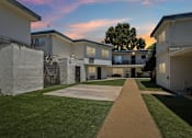 Thumbnail 1 of 10 - A pathway leads through a grassy area between two rows of houses.