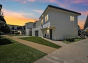 Thumbnail 2 of 10 - A row of white houses with a sunset in the background.