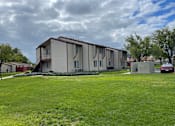 Thumbnail 3 of 7 - a white apartment building with a green yard and a cloudy sky