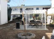 Thumbnail 6 of 10 - A patio with a table and chairs is surrounded by white buildings.