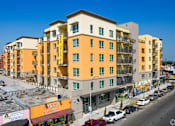 Thumbnail 2 of 17 - A street view of a yellow and white apartment building with cars parked in front.