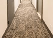 Thumbnail 5 of 11 - A long hallway with doors on both sides and a carpeted floor.
