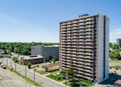Thumbnail 1 of 24 - A tall building with many windows is surrounded by a parking lot.