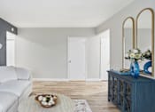 Thumbnail 12 of 34 - A white couch with blue pillows sits in a room with a wooden floor and a mirror on the wall.