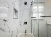 Thumbnail 34 of 60 - A white bathroom with a marble wall and a glass shower door.