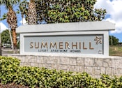 Thumbnail 2 of 15 - A sign for Summerhill Luxury Apartment Homes is displayed in front of a tree.