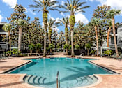 Thumbnail 5 of 15 - A swimming pool surrounded by palm trees and a building in the background.
