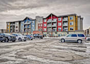 Thumbnail 23 of 72 - A parking lot with cars and a multi-story apartment building in the background.