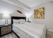 Thumbnail 9 of 27 - A bedroom with a bed, nightstand, and a painting on the wall.