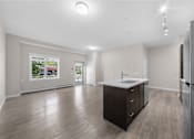 Thumbnail 12 of 25 - an empty living room with a kitchen with a refrigerator and a sink