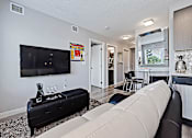 Thumbnail 12 of 27 - A black sofa with a white cushion is in the foreground of a well-lit living room.