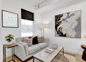 Thumbnail 1 of 78 - A living room with a grey couch, a coffee table, a side table, a lamp, and a painting on the wall.