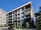 Thumbnail 64 of 78 - A modern multi-story apartment building with balconies and a parking lot in front.