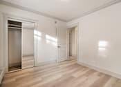 Thumbnail 35 of 219 - A room with a wooden floor and white walls, with a door on the left and a window on the right.