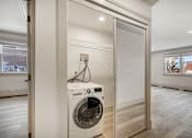 Thumbnail 71 of 219 - A white washing machine is in a small room with a door open.