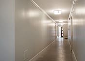 Thumbnail 209 of 219 - A long hallway with lights on the ceiling and a door at the end.